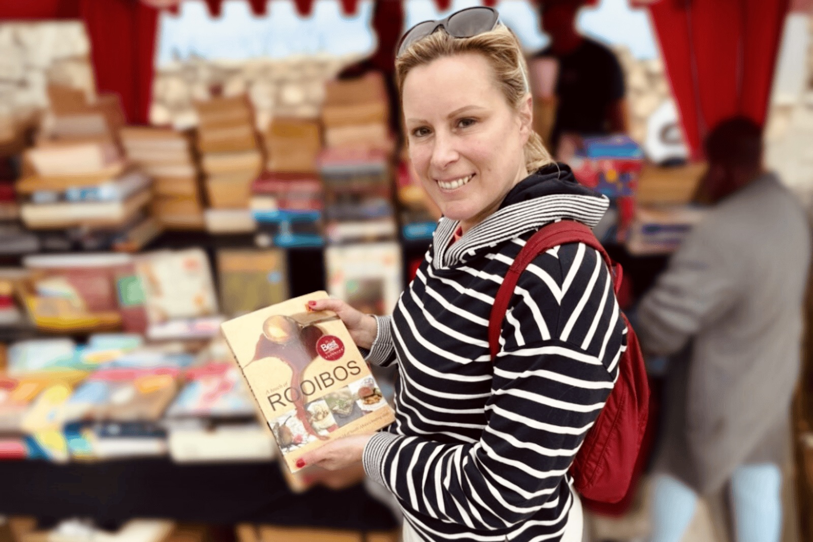 Heleen toont een lokaal kookboek over rooibos op een markt in Zuid-Afrika.